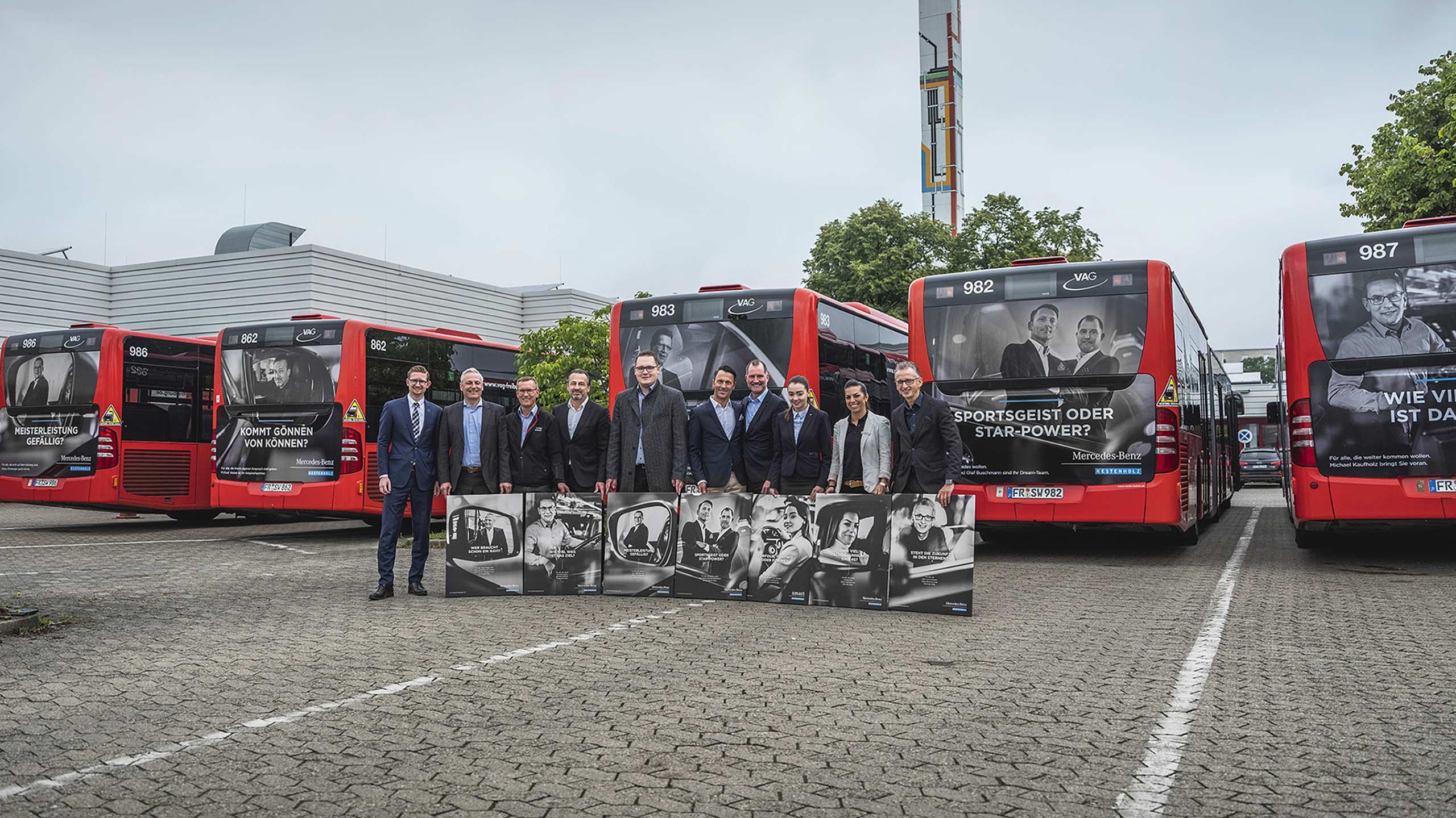 Die Personen aus der Kampagne stehen vor den Bussen mit ihren jeweiligen Motiven als Poster vor sich
